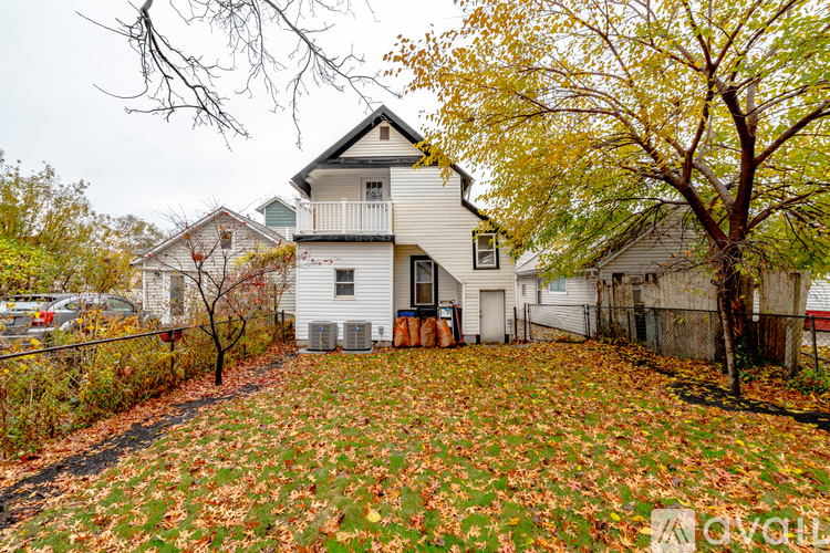 A white house with a grey roof surrounded by a fence and trees with yellow leaves.