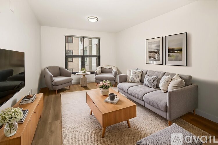 A living room with a grey couch, a wooden coffee table, and a large window.