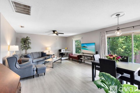 A living room with a grey couch, a black chair, a dining table with chairs, and a painting on the wall.