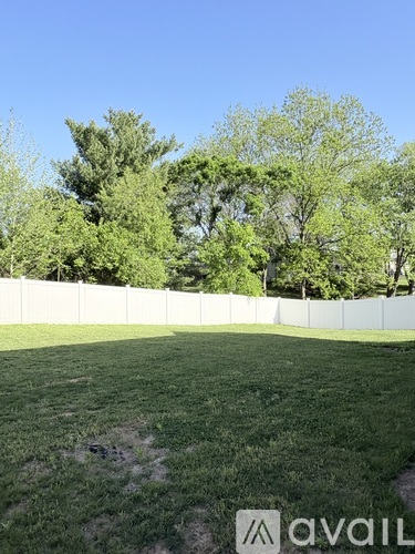 A grassy field with a white fence and trees in the background.