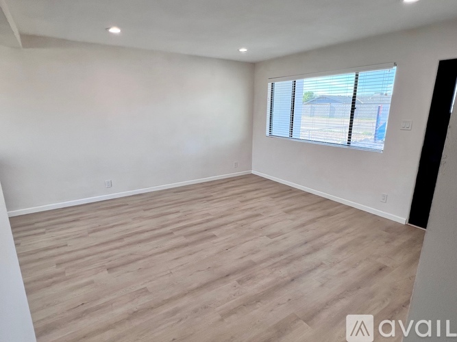 A spacious room with wooden flooring and a window with blinds.