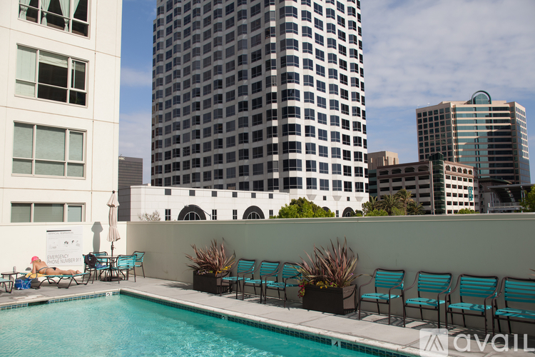A pool with chairs and plants on a patio with tall buildings in the background.