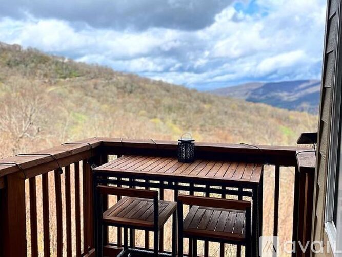 A wooden table and two chairs on a balcony overlooking a mountainous landscape.