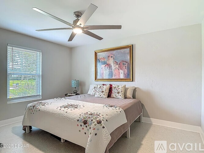 A bedroom with a bed, a ceiling fan, and a painting on the wall.