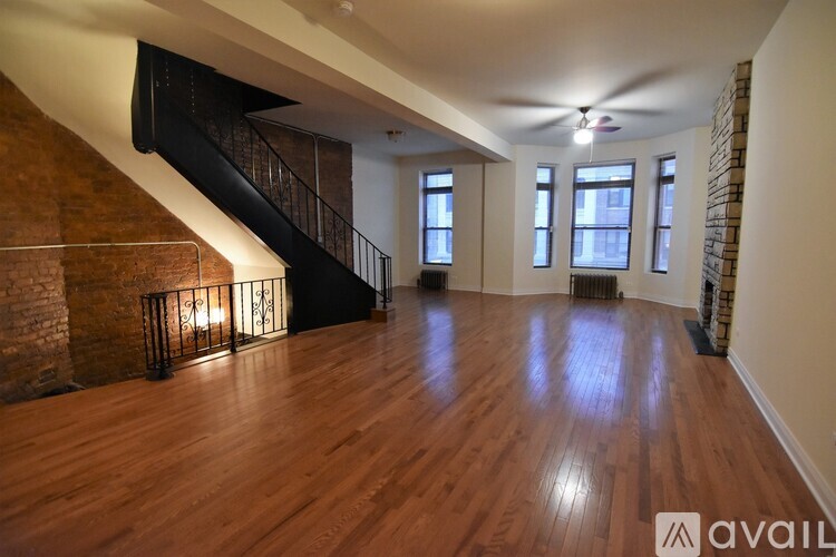 A spacious room with wooden floors and a staircase with a metal railing.