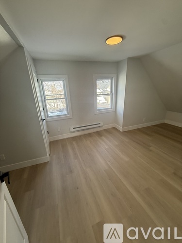 A room with wooden flooring and two windows.
