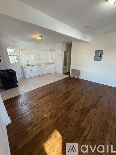 A room with wooden flooring and a kitchen area in the background.