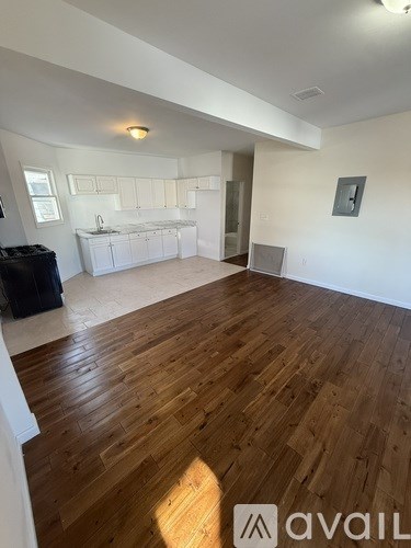 A room with wooden flooring and a kitchen area in the background.