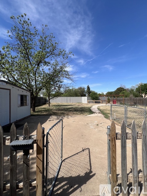 A fenced area with a white building and a tree in the background.