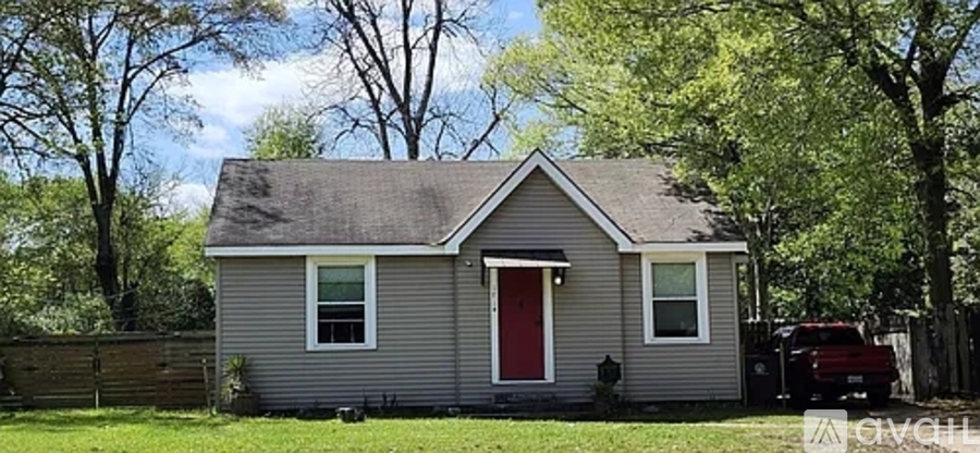 A small house with a red door is surrounded by trees.