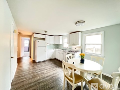 A kitchen with a table and chairs in the foreground and a refrigerator, microwave, and oven in the background.