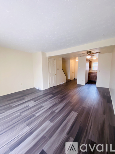 A room with wooden flooring and a staircase in the background.