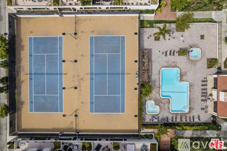 Two tennis courts are surrounded by a pool and parking lot.