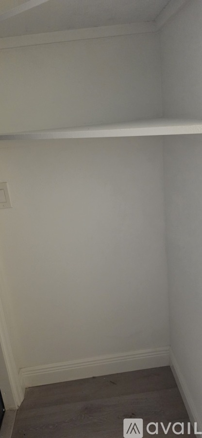 A white wall with a light switch and a wooden floor.