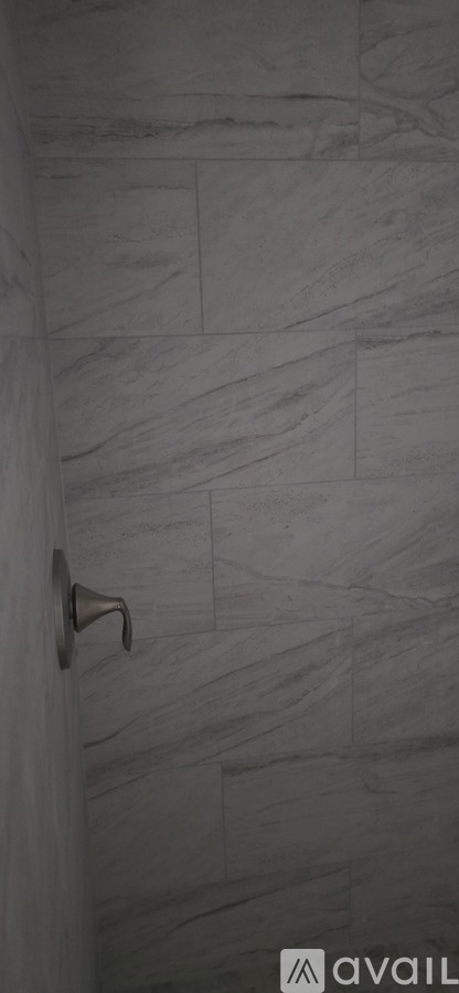 A shower with a grey tile wall and a silver shower head.