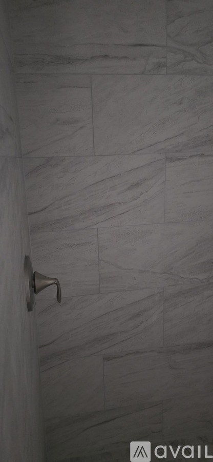 A shower with a grey tile wall and a silver shower head.