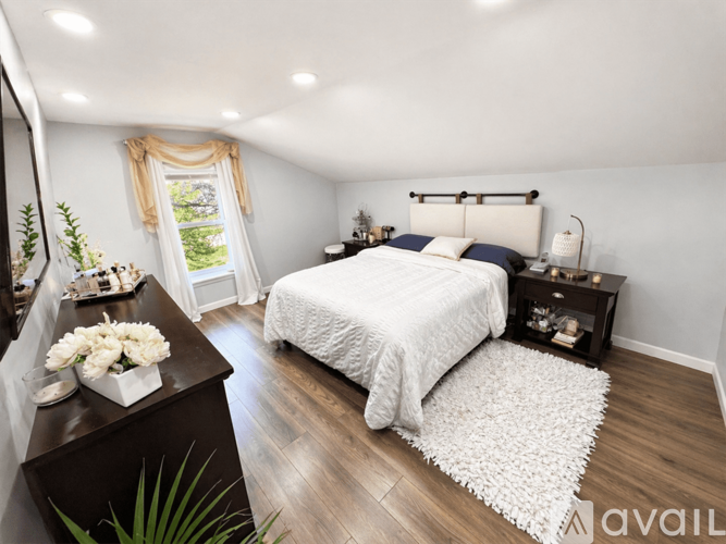 A bedroom with a white bed and a wooden dresser.