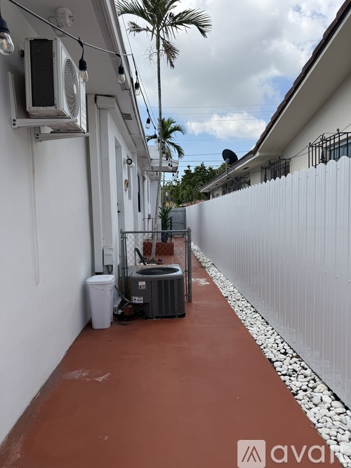 A red pathway leads to a white building with a palm tree in the background.