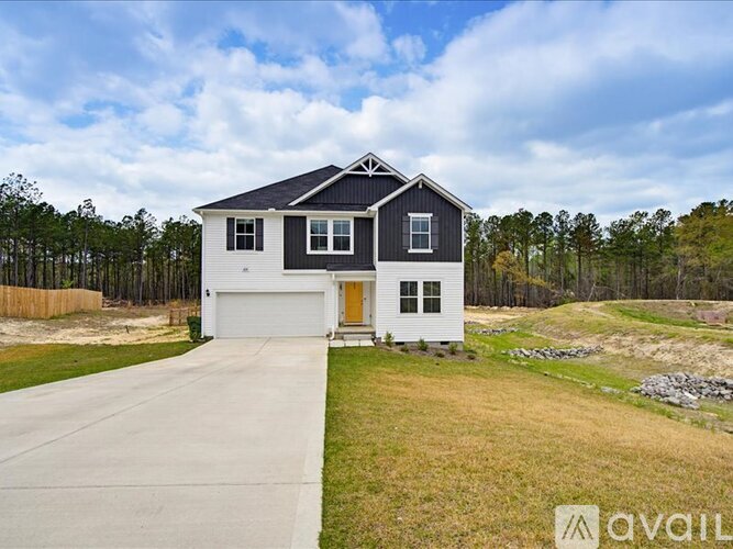 A two-story house with a garage is situated in a grassy area with trees in the background.