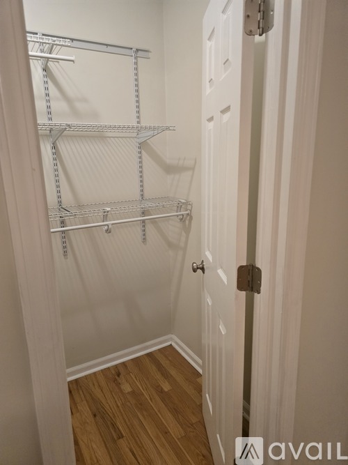 A white door with a silver handle is open to a hallway with a white wall and a white shelving unit.