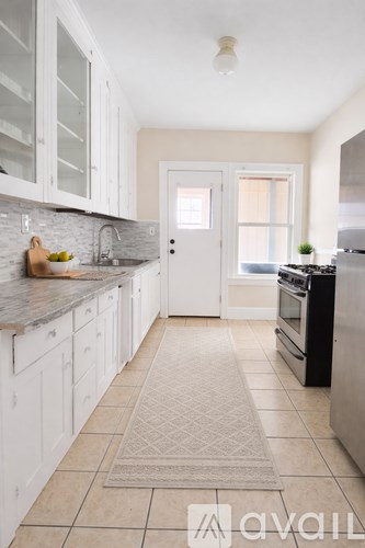 A kitchen with white cabinets and a beige rug on the floor.