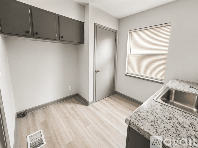 A kitchen with a sink, wooden flooring, and a window with blinds.