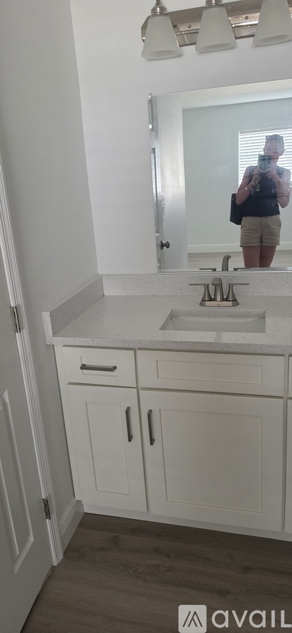 A person is taking a selfie in a bathroom with a white sink and cabinets.