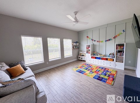 A living room with a grey couch, a ceiling fan, and a rug on the floor.