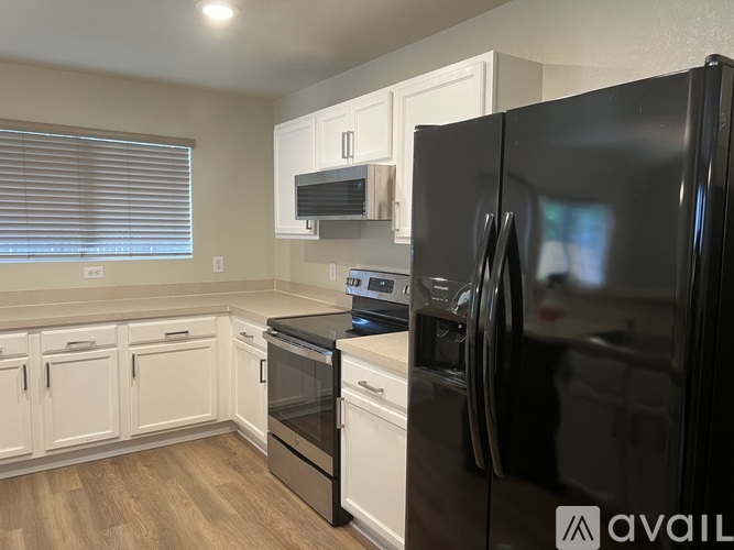 A black refrigerator is in the foreground of a kitchen with white cabinets and a stove.