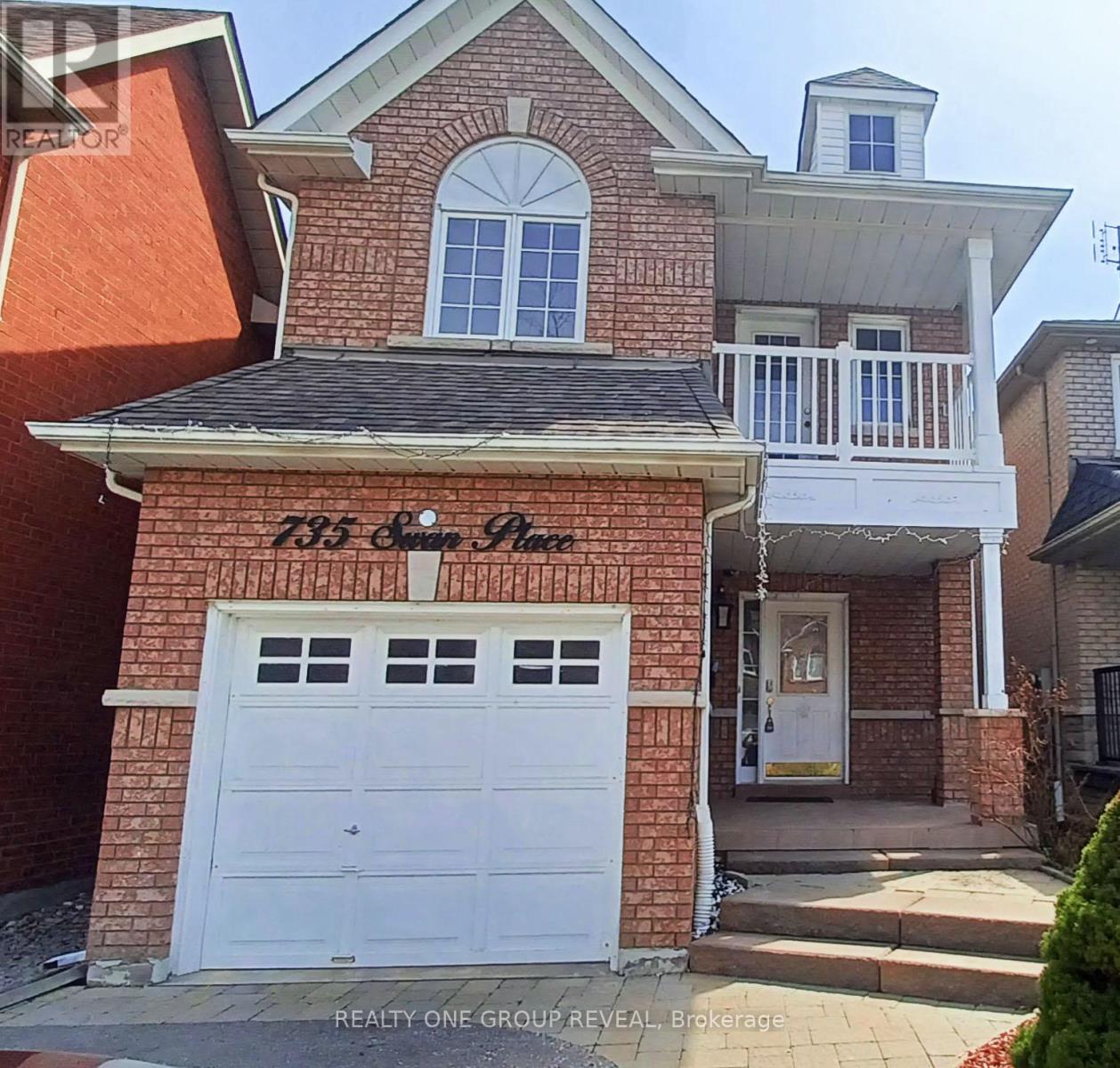 A house with a white garage door and a sign that says "REALTY ONE GROUP REVEAL Brokerage".