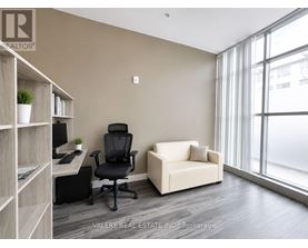 A room with a desk, chair, and couch with a window in the background.