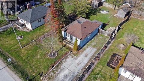 A blue house with a brown roof is surrounded by a grassy area and trees.
