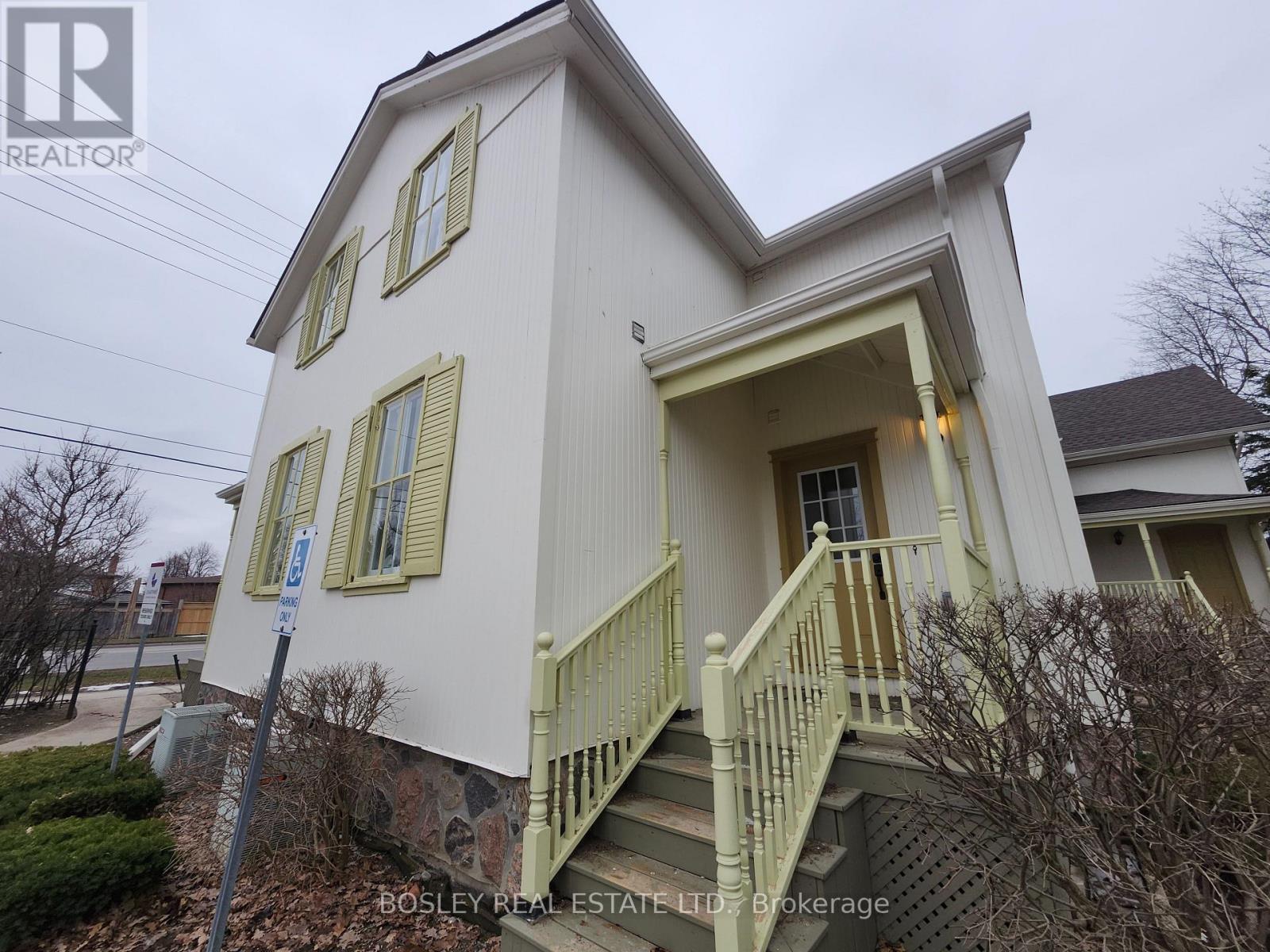 A white house with a green staircase and a sign that says "Bosley Real Estate LTD Brokerage".
