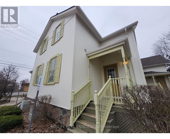 A white house with a green staircase and a sign that says "Bosley Real Estate LTD Brokerage".