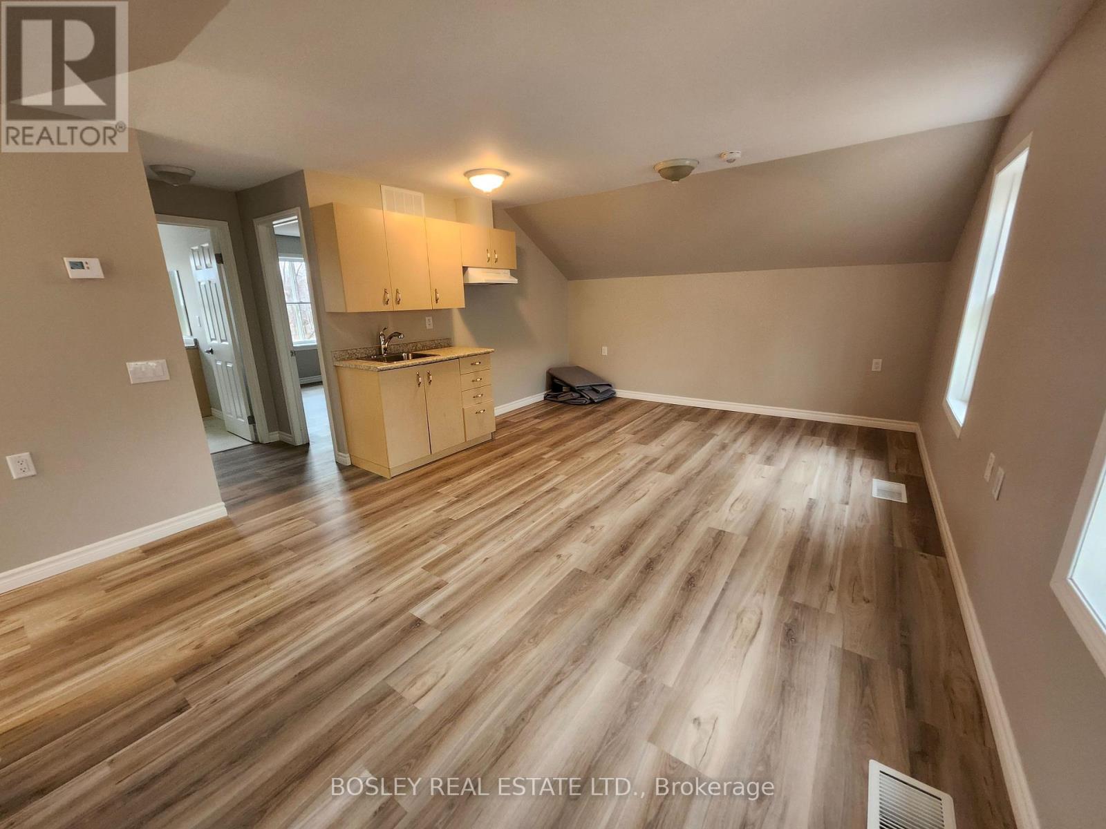 A spacious room with wooden flooring and a kitchen area in the background.