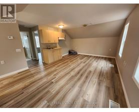 A spacious room with wooden flooring and a kitchen area in the background.