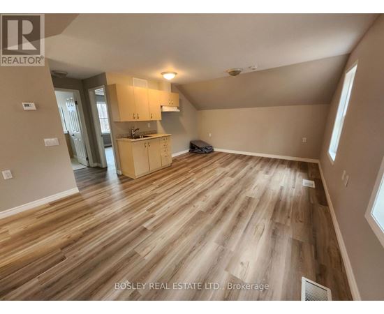 A spacious room with wooden flooring and a kitchen area in the background.