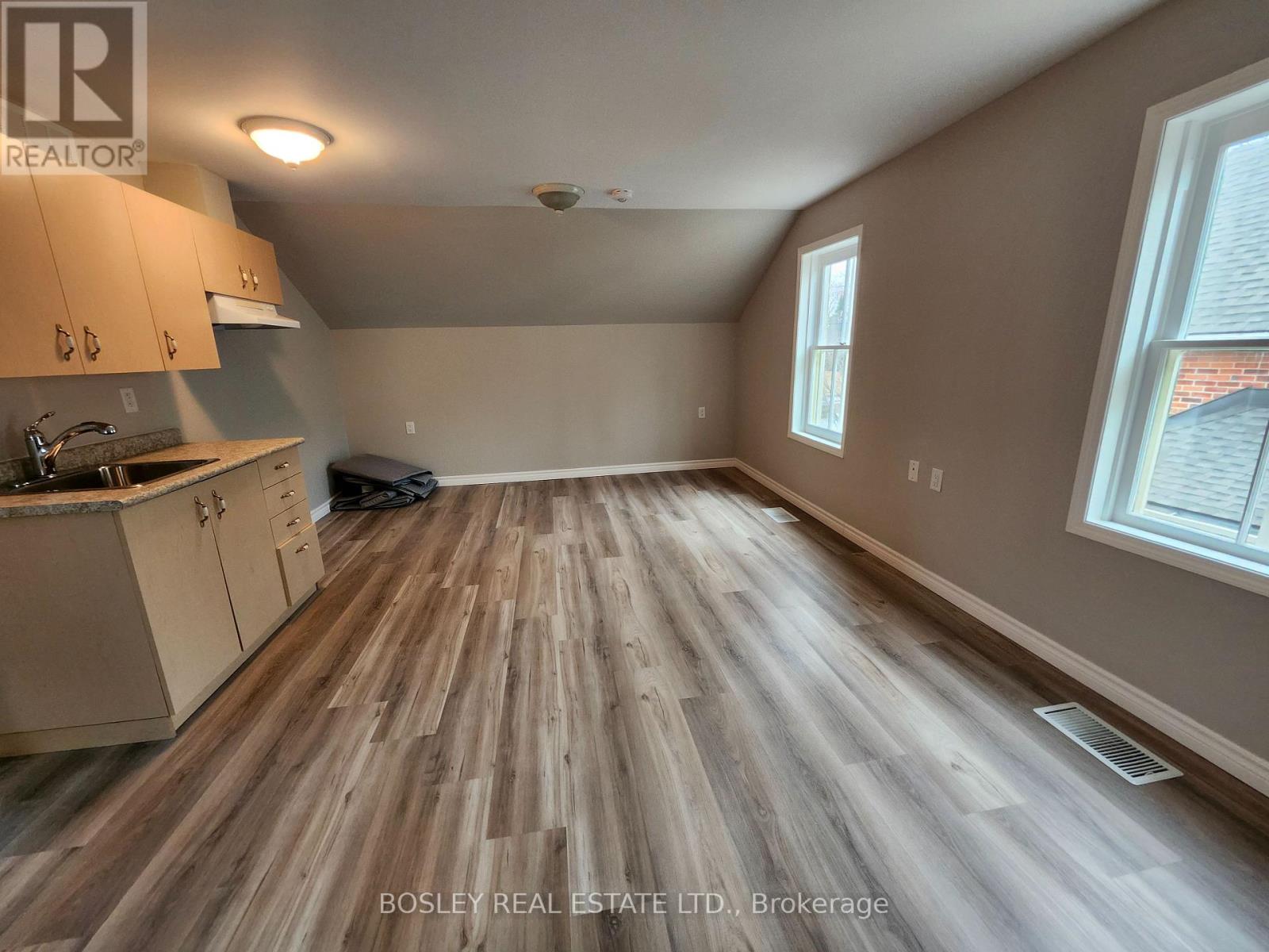 A room with wooden flooring and a kitchen area with cabinets and a sink.