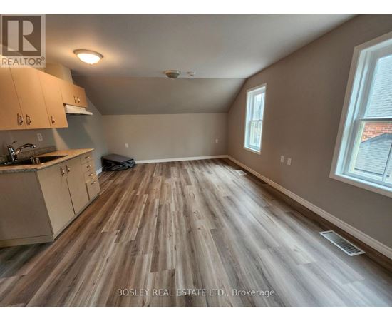 A room with wooden flooring and a kitchen area with cabinets and a sink.