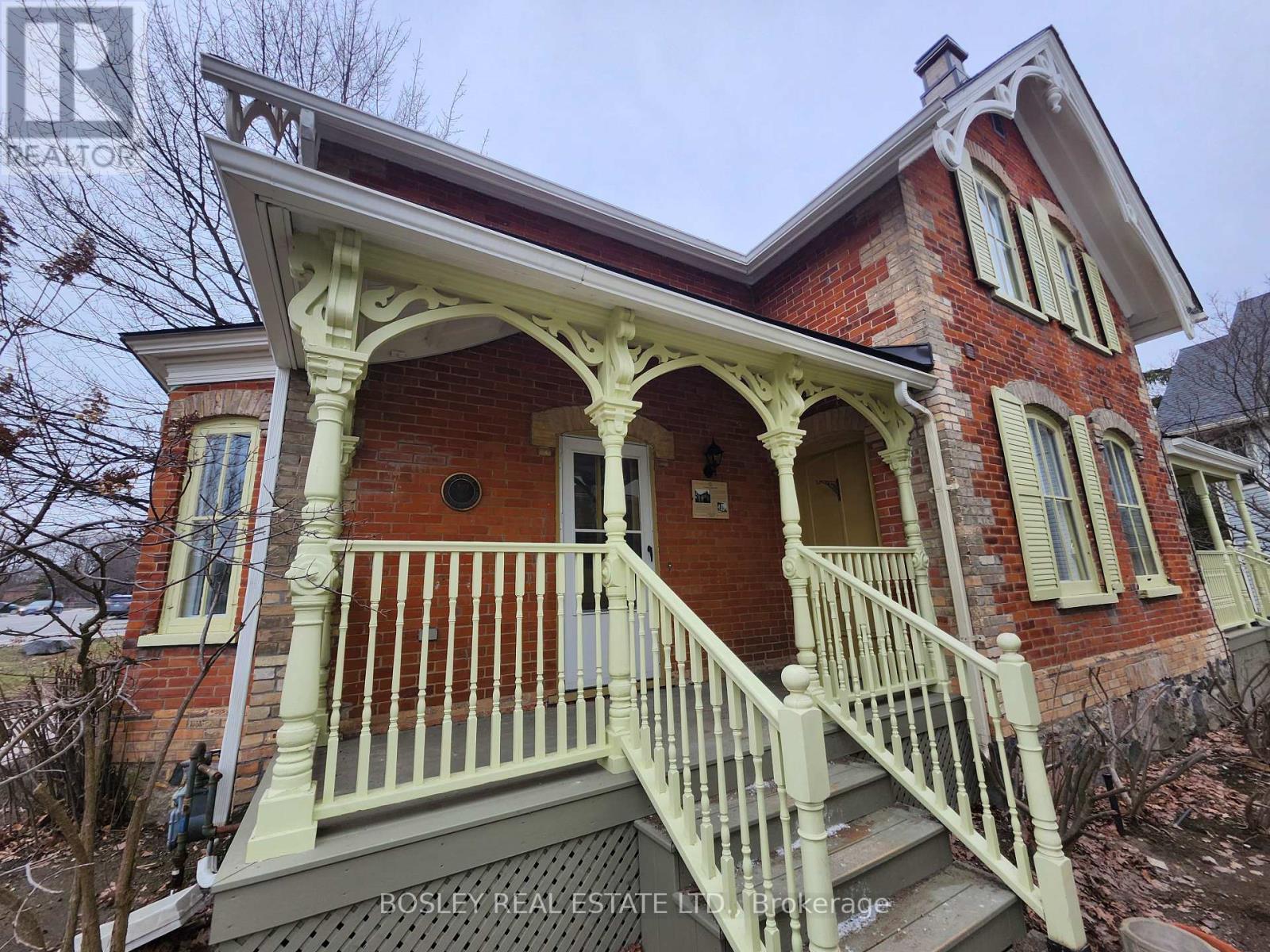 A red brick house with a white porch and a sign that says Rosley Real Estate.
