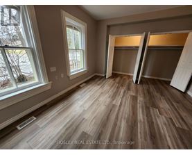 A room with wooden flooring and a window showing trees outside.