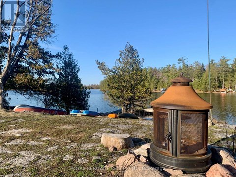 A rustic lantern sits on a rock by a lake with trees and boats in the background.