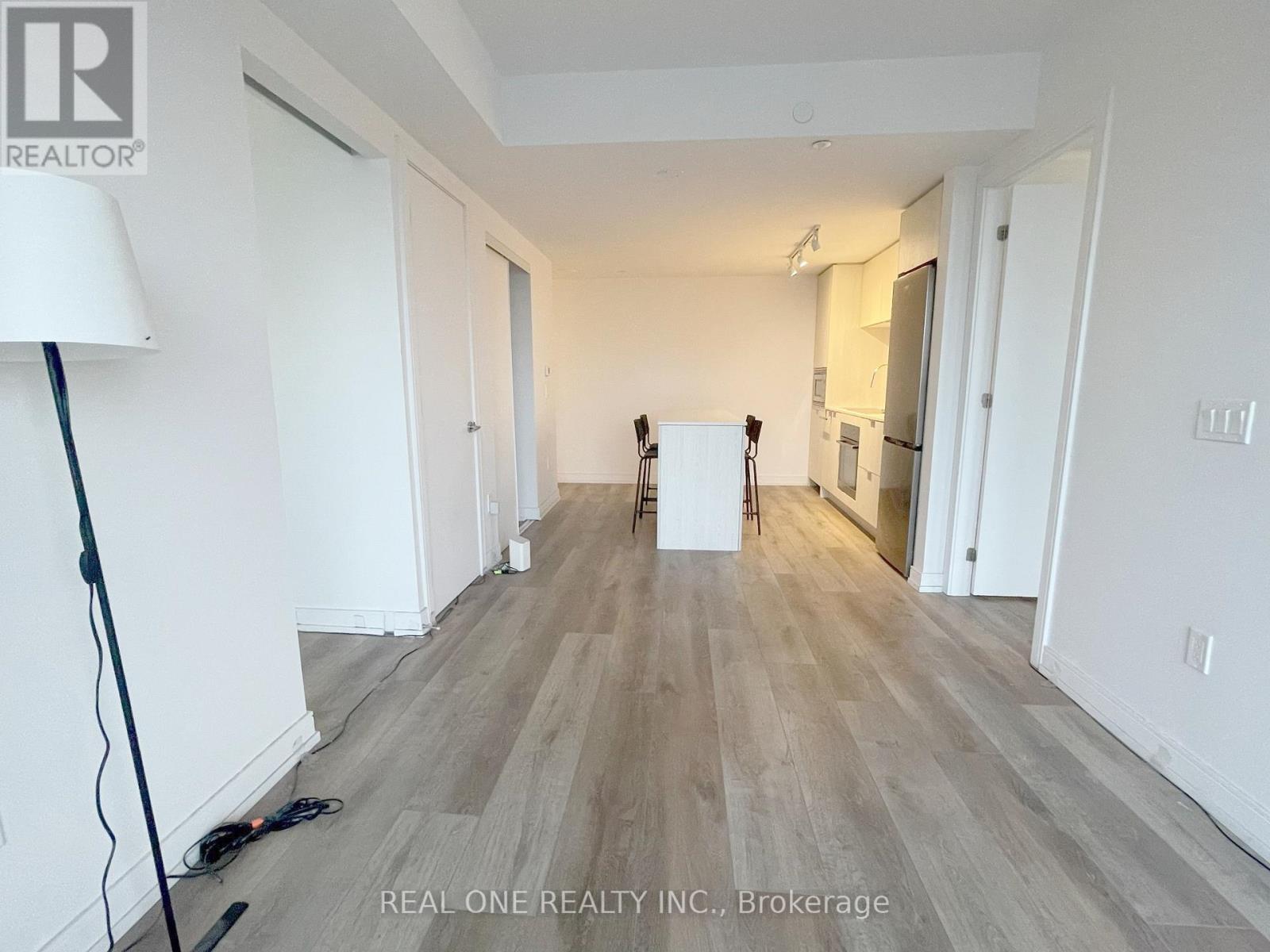 A room with white walls and wooden flooring, with a lamp on the left and a white box in the middle.