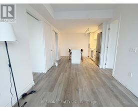 A room with white walls and wooden flooring, with a lamp on the left and a white box in the middle.