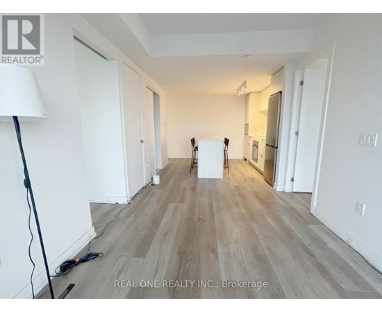 A room with white walls and wooden flooring, with a lamp on the left and a white box in the middle.