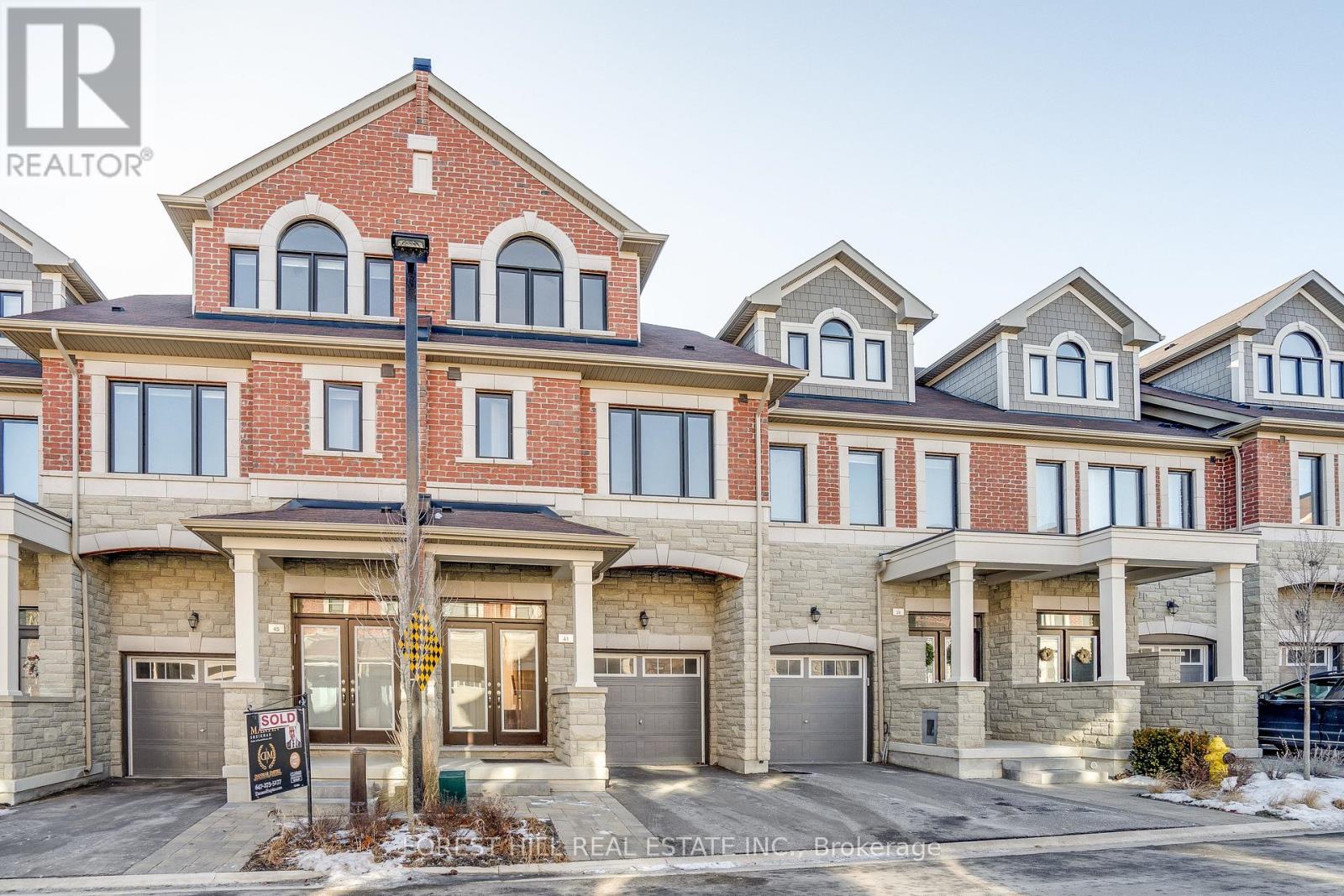 A real estate sign is displayed in front of a row of houses.