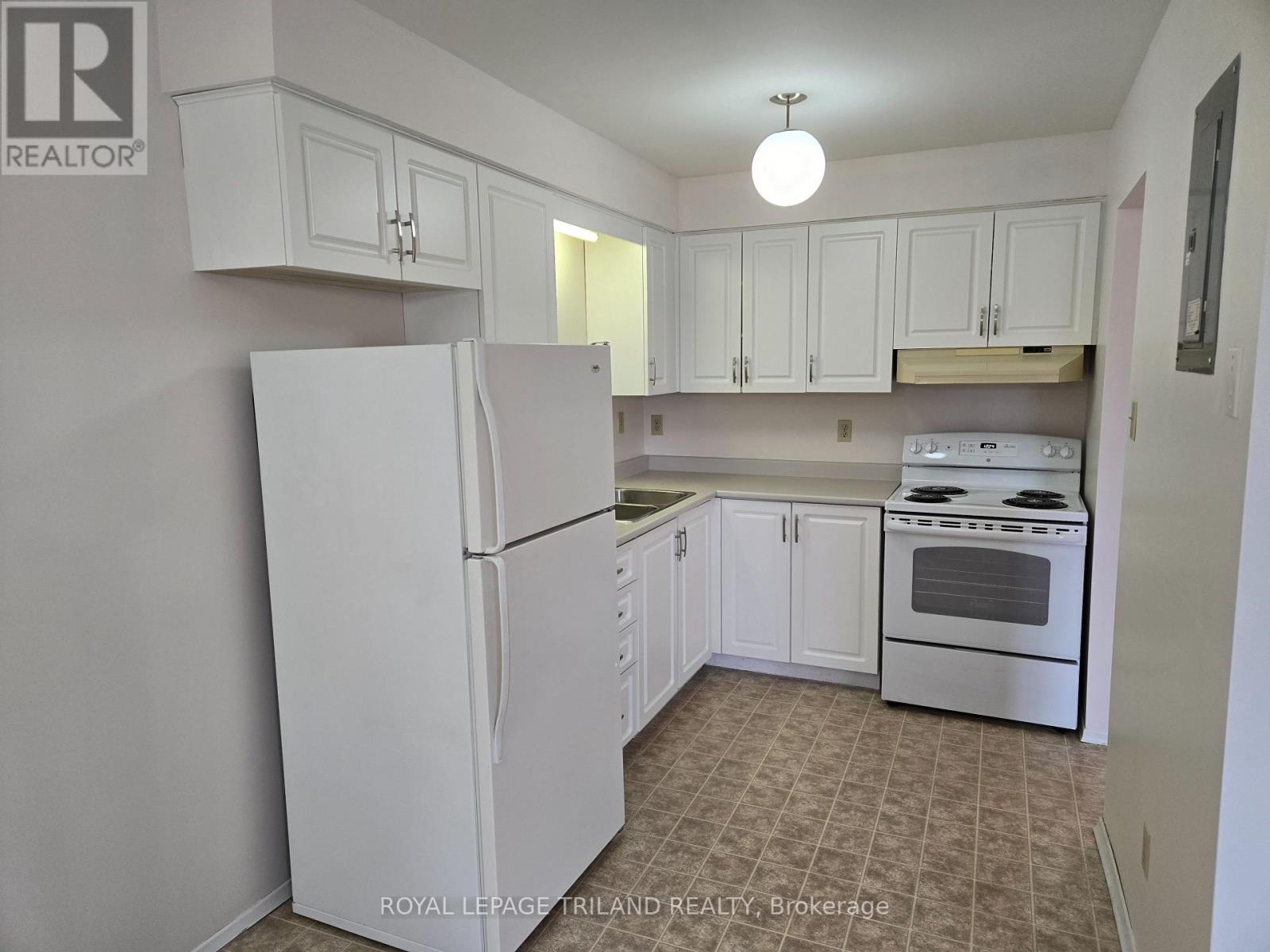 A white refrigerator stands in a kitchen with white cabinets.