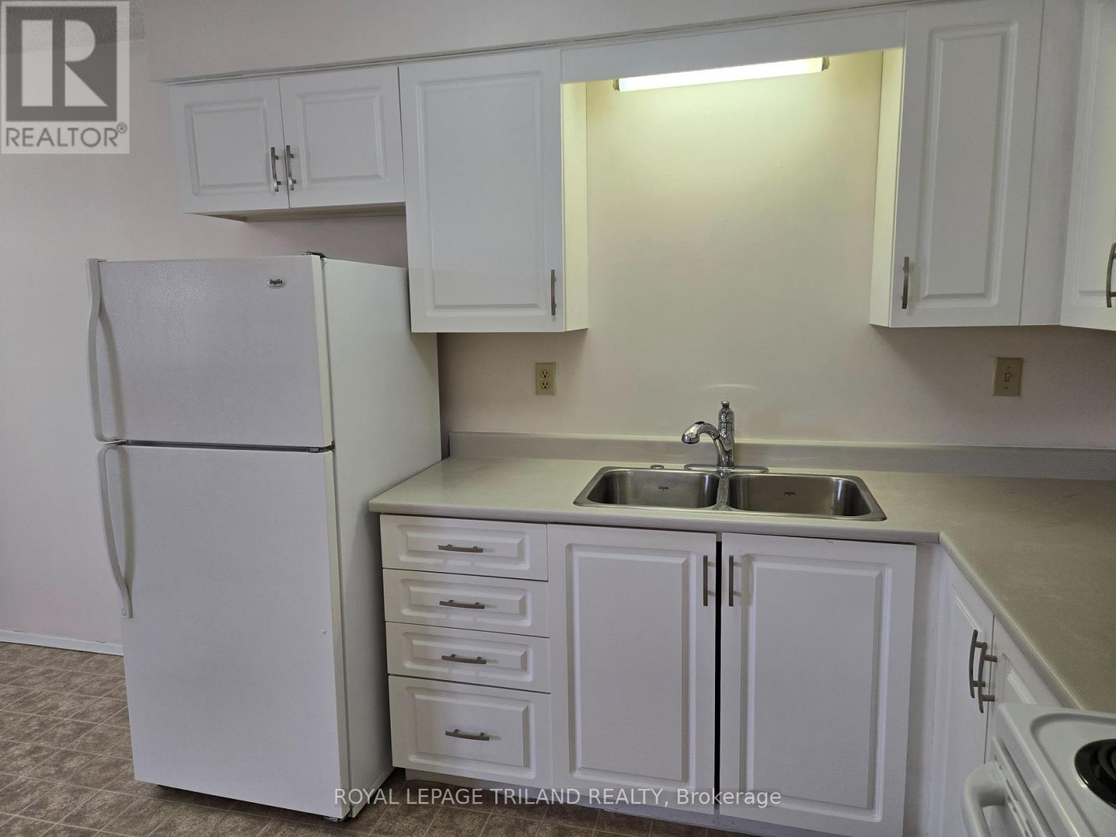 A white refrigerator is in a kitchen with white cabinets.