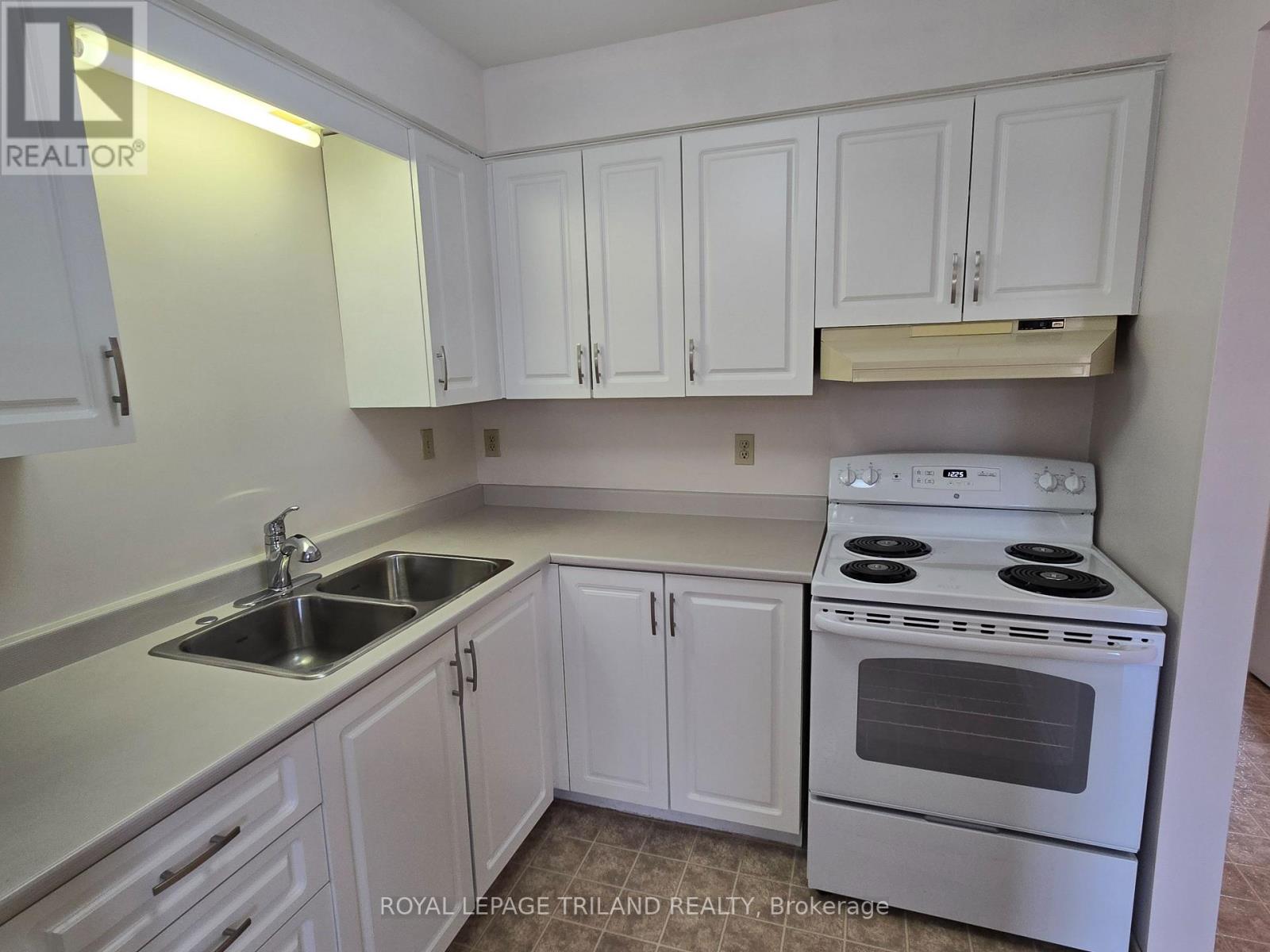 A white kitchen with a stove, sink, and cabinets.