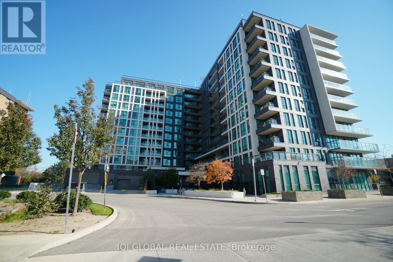 A modern multi-story building with a glass facade and a parking lot in front.